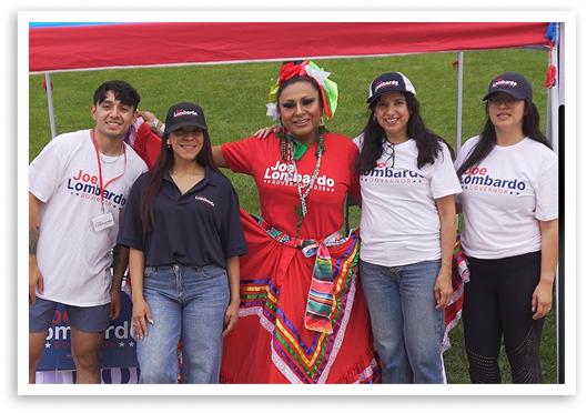 Joe Lombardo campaign volunteers and a person in traditional Mexican dress posing at an outdoor community event.